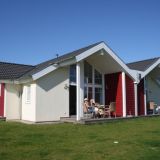 Ein kleines flaches Häuschen mit gelber und roter Färbung außen. Auf der Terrasse sitzen Gäste.