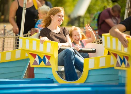 In der Attraktion Koggenfahrt sitzen eine Frau und ein Mädchen. Das Mädchen winkt.