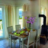 Gedeckter Esstisch vor einer Fensterfront. Hintergrund: Eine Couch mit Sesseln und einen Couchtisch.