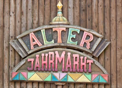 Das Schild des Alter Jahrmarkts. Es ist aus Holz. Die Deko-Elemente und die Schrift sind bunt.