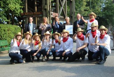 Menschen in zwei Reihen. Hintere Reihe steht, davon fünf in formeller und Rest in Western Kleidung.