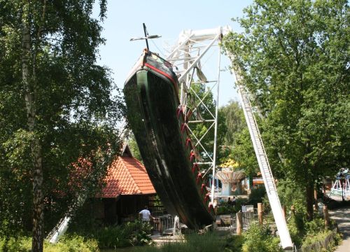 Die Attraktion Schiffschaukel schwingt sich nach oben. Der Boden des Schiffs ist dunkelgrün.