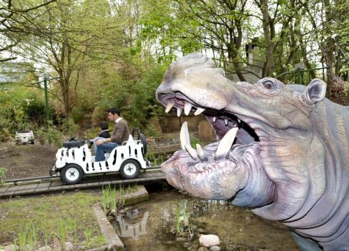 Hinter einem Flusspferd fahren ein Mann und ein Junge mit einem Jeep in der Attraktion Safari-Jeeps.