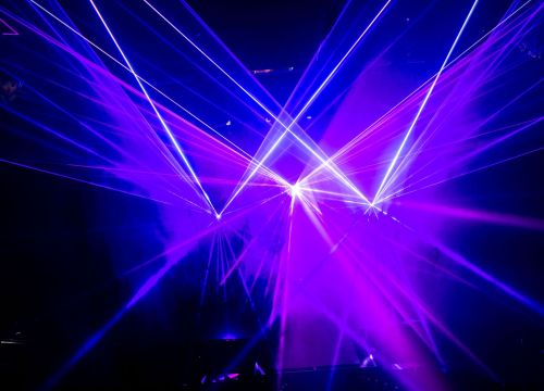 Im Nebel der Lasershow zeigen rosa und weiße Laserstrahlen in die Luft. Sie bilden ein W.