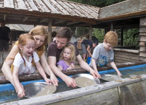 Eine Familie beim Goldwaschen. Sie habe insgesamt 3 Schalen im Wasser. In allen Schalen ist Sand.