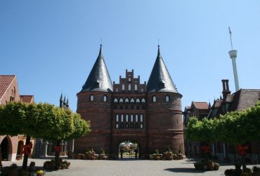 Das Holstentor aus Lübeck von vorne. Davor stehen viele bepflanzte Blumentöpfe.