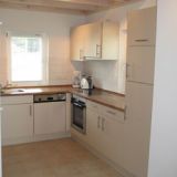 Eine Küchenzeile mit weißer Front. Mit Spülmaschine, Backofen, Herdplatte und Spüle.