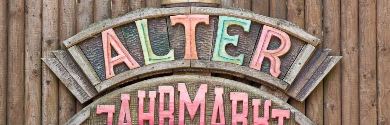 Das Schild des Alter Jahrmarkts. Es ist aus Holz. Die Deko-Elemente und die Schrift sind bunt.