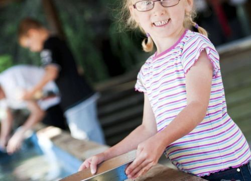 Ein Mädchen mit einer Schale beim Goldwaschen. Das Mädchen schaut hoch und lächelt.