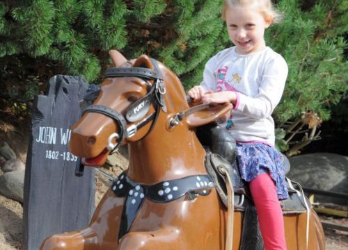 Ein Mädchen hält sich am Pferd fest. Das Mädchen reitet über die Anlage der Attraktion Pony Post.