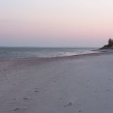 Ein Strand an der Ostsee. Er ist in Abendstimmung getaucht. Der Himmel ist weiß und rosafarben.