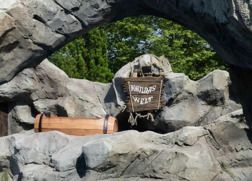 Unter einem Bogen sieht man den Namen der Attraktion: Awildas Welt. Ein Boot fährt daran vorbei.