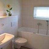 Ein Badezimmer mit Badewanne, Toilette und Waschbecken. Es hat ein kleines Fenster.