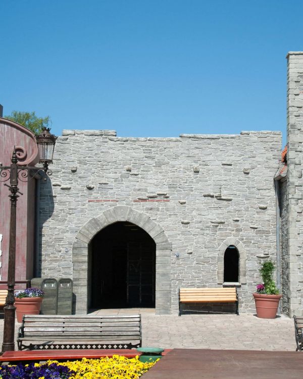 Blick auf die Arkaden Visby. Die Stadtmauer von Visby in grau. Ein Eingang führt unter die Arkaden.