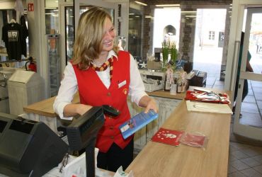 Eine junge Frau steht an der Kasse des HANSE-Kontors und kassiert Ware ab. Sie lächelt dabei.