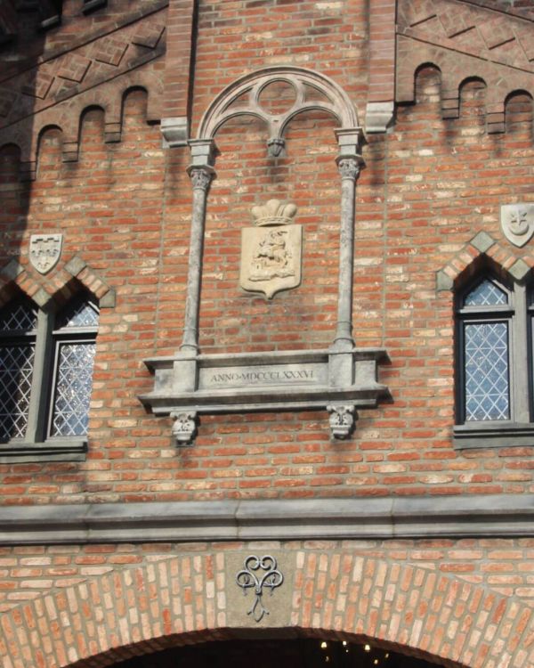 Ein Gotischer Bogen mit einem Wappen in der Mitte. Links und rechts daneben sind Fenster.