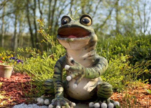 Der Frosch auf der Anlage der Attraktion Blumenmeer-Bootsfahrt lächelt und streckt den Arm aus.