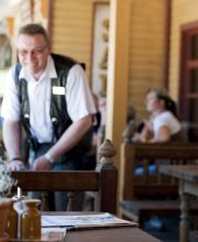 Eine Frau sitzt am Tisch des Saloon New Chance. Sie lächelt. Der Kassierer hinter ihr auch.
