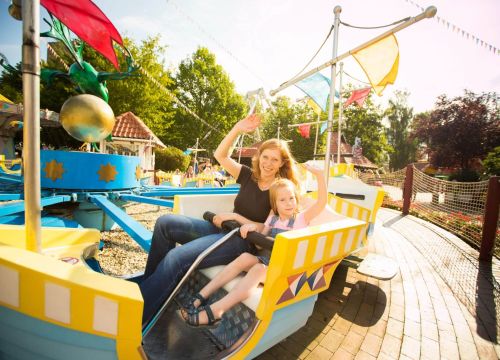 In der Attraktion Koggenfahrt winken eine Frau und ein Mädchen. Die Gondel hat einen roten Wimpel.