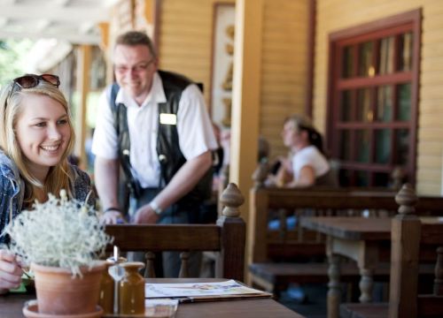 Eine Frau sitzt am Tisch des Saloon New Chance. Sie lächelt. Der Kassierer hinter ihr auch.