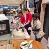 Drei junge Frauen in HANSA-PARK Arbeitskleidung bereiten Speisen hinter einem Tresen zu.