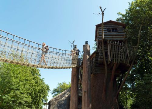 Die Apachen Lodge und Hängebrücke von unten. Zwei Mädchen laufen über die Hängebrücke.