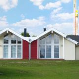 Ein kleines flaches Häuschen mit gelber und roter Färbung außen. Auf der Terrasse sitzen Gäste.