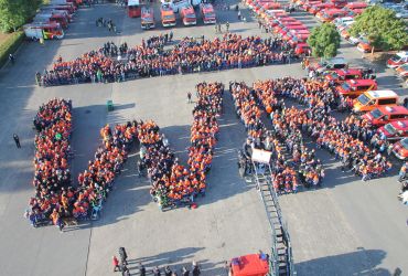 Auf dem Parkplatz haben Feuerwehrleute ein großes Wir gebildet. Darüber steht noch mehr Menschen.