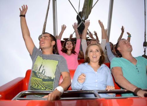 Gäste freuen sich in der Attraktion Schiffschaukel. Sie lachen und haben die Arme hoch.