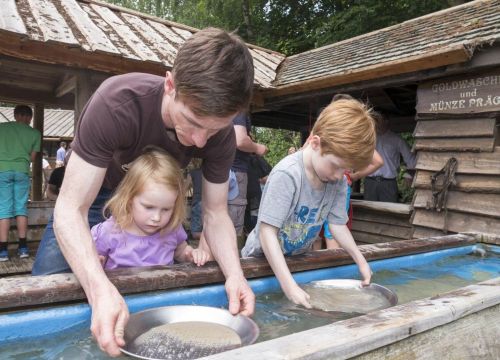 Ein Mann und zwei Kinder beim Goldwaschen. Der Mann hält die eine Schale. Das eine Kind die andere.