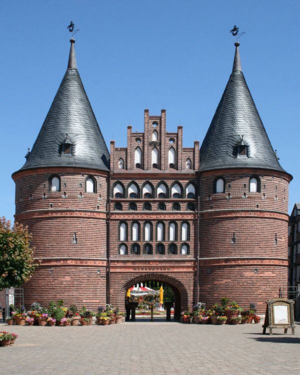 Das Holstentor aus Lübeck von vorne. Davor stehen viele bepflanzte Blumentöpfe.