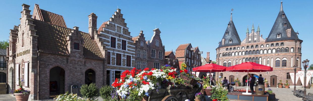 Die hanseatischen Arcaden. Davor steht ein Karren mit Blumen. Das Holstentor dahinter.