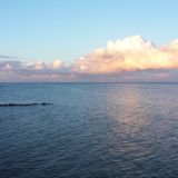 Die Ostsee. In regelmäßigen Abständen sind Molen zu sehen. Der Himmel ist blau mit ein paar Wolken.