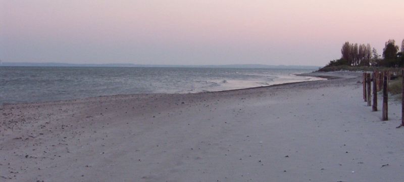 Ein Strand an der Ostsee. Er ist in Abendstimmung getaucht. Der Himmel ist weiß und rosafarben.