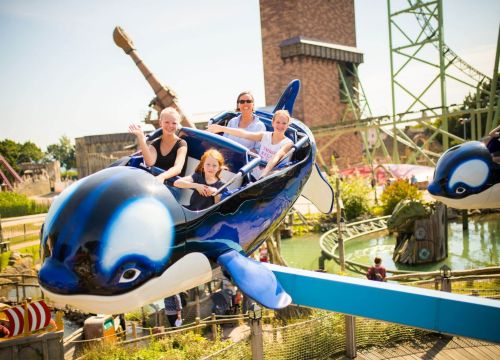 Ein Orca der Attraktion Flying Orca mit vier Gästen drin. Der Orca ist oben in der Luft.