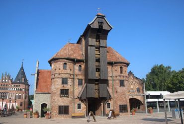 Das Krantor von Danzig von vorne. Der Bereich des Krans ist im Fokus. Das Holstentor dahinter.