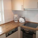 Die Kaffeemaschine, Toaster, Spülmaschine, Backofen, Herdplatte und Spüle im Fokus der Küchenzeile.