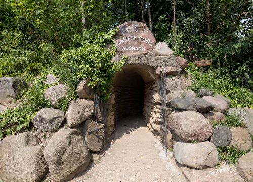 Der Ausgang der Bärenhöhle. Aus bewachsenen Steinen kommt man durch ein geöffnetes Tor nach draußen.