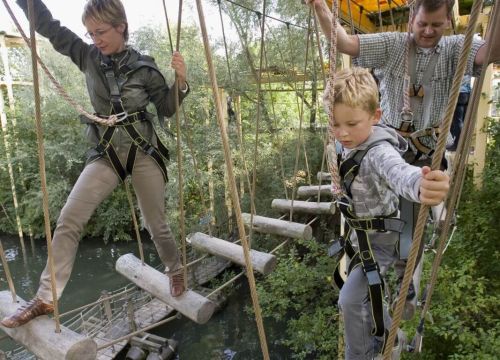 Eine Frau, ein Mann und ein Junge mit Klettergurten benutzen den Hochseilgarten Navajo Trail.