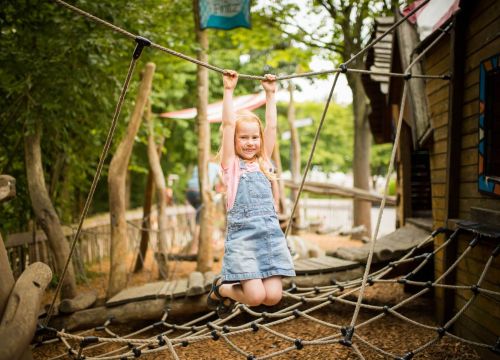 Ein Mädchen hängt an dem Seil des Netztes im Niedrigseilgarten. Das Netz ist an einem kleinen Häuschen.
