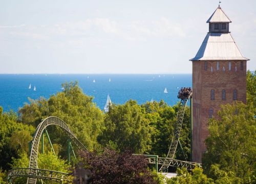 Die Attraktion Flucht von Novgorod mit Turm erhebt sich aus Bäumen. Die Ostsee ist im Hintergrund.