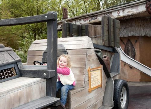 Auf dem Dschungel Jeep aus Holz sitzt ein Mädchen. Es hält sich am Lenkrad fest.