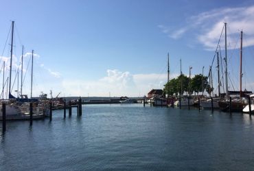 Ein Hafen. Es liegen Segelboote am Hafen an. Der Himmel ist blau.