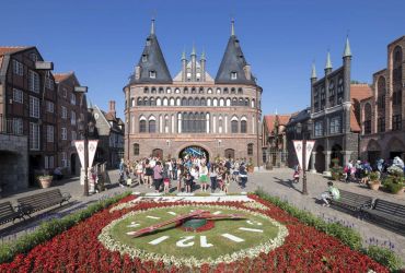 Eine Gruppe von jungen Menschen hinter der Blumenuhr und steht vor dem Holstentor.