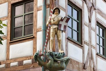 Eine Figur mit einer Stechlanze und einem Schild mit einem Dach.