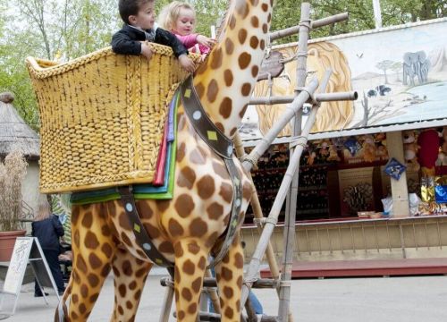 Die Giraffe Kira seitlich. Die Kinder haben die Arme über den Korbrand und streicheln die Giraffe.