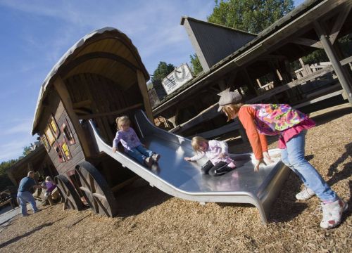 Die Postkutsche von hinten. Zwei Mädchen benutzen die Rutsche. Eines steht daneben.