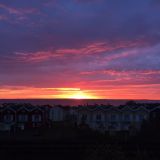 Über den kleinen Häuschen des Resorts geht die Sonne rosafarben unter. Darunter das Meer.