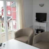 Zwei Sesseln und ein Couchtisch. Im Hintergrund ein Tisch mit einem Fernseher.