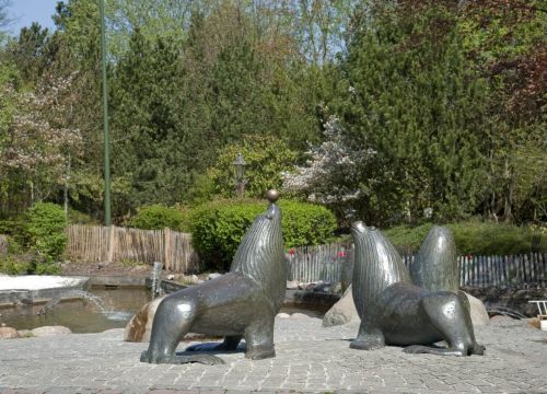 Vier Seelöwen aus Bronze vor einem Wasserspiel. Einer der Seelöwen hat einen Ball auf der Nase.